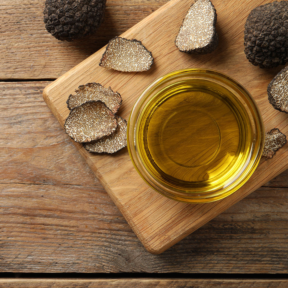 a bowl of oil and black truffles on a cutting board