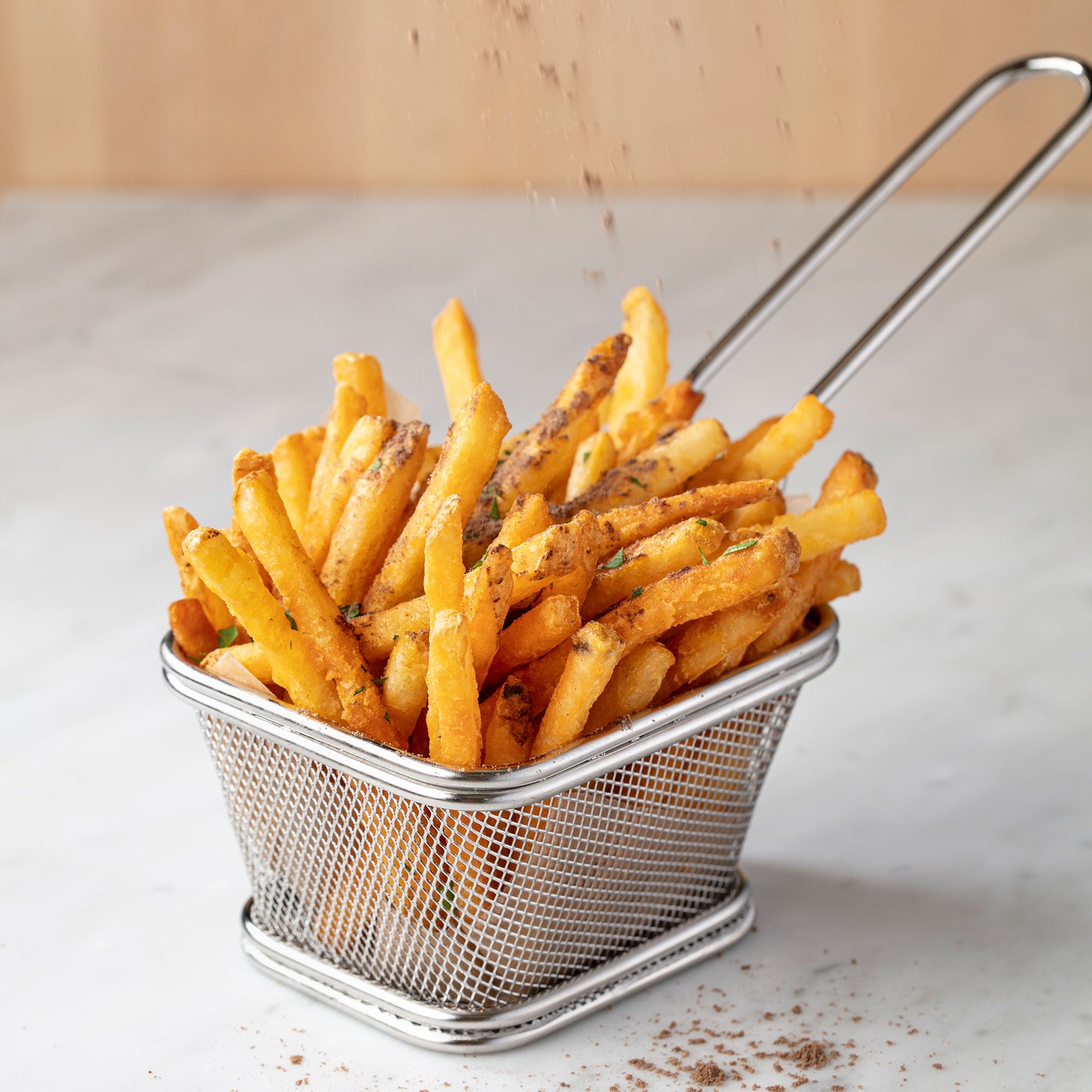 a basket of french fries with a ladle sprinkled with seasoning